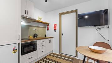A compact kitchen with white cabinets, a microwave, a coffee maker, and a wooden table with a bowl.