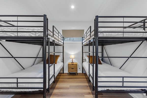 Una habitación con literas, una mesita de noche de madera con lámpara y una ventana con persianas.