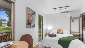 Een moderne slaapkamer met een groot bed, een houten tafel en een stoel. Op de muur hangt een schilderij en er is een raam met uitzicht op de omgeving.