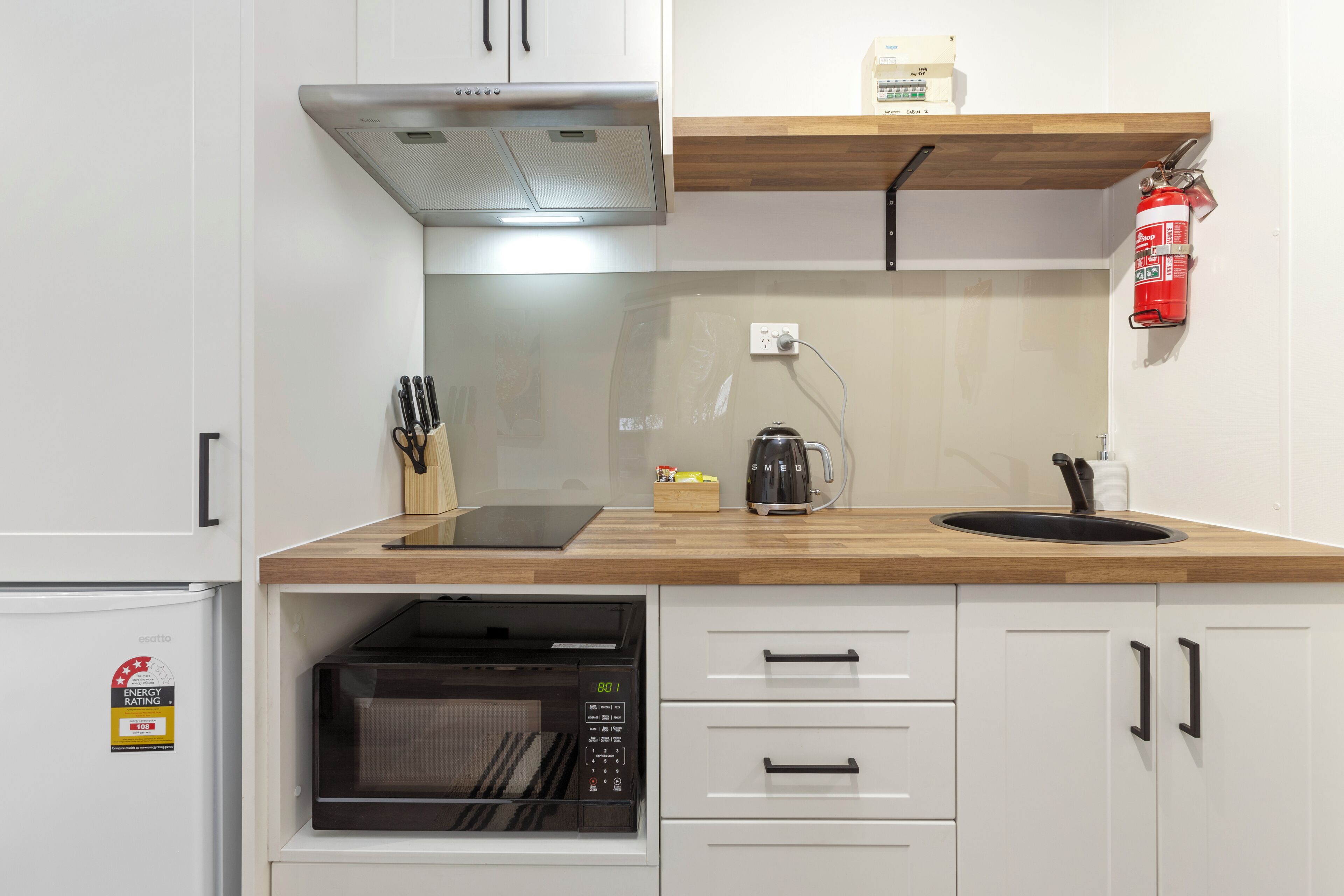 A modern kitchen with white cabinets, a wooden countertop, a built-in microwave, and a coffee maker.