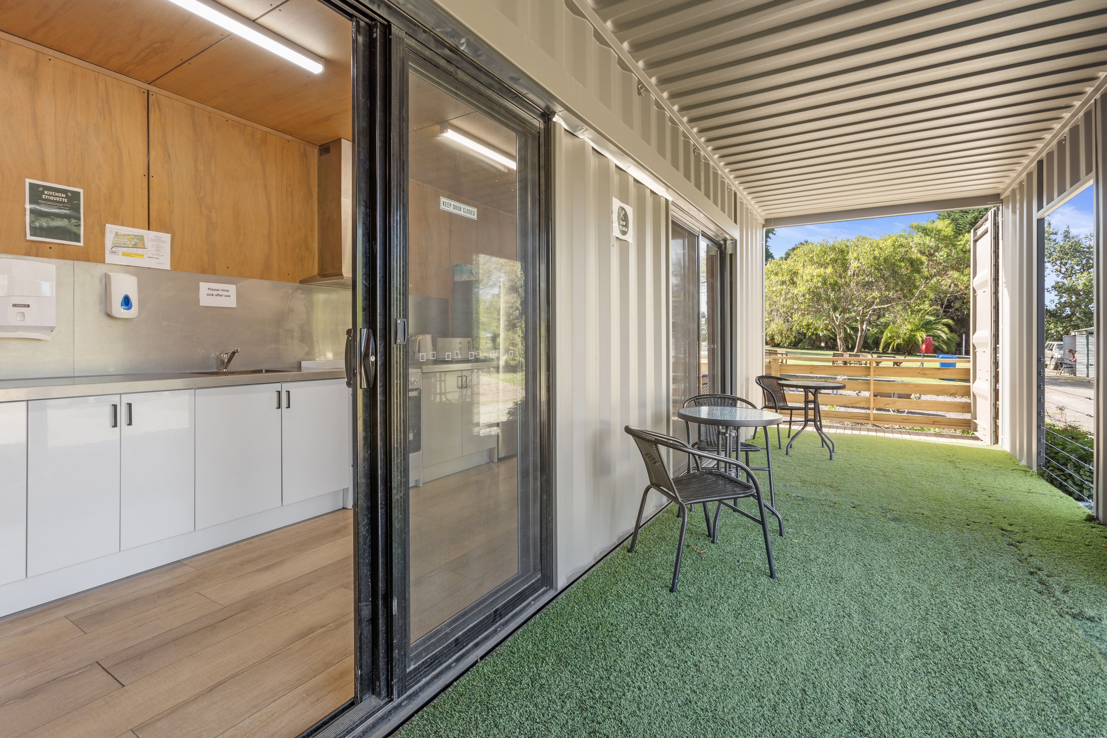 A modern kitchen with white cabinets and a glass door leading to an outdoor patio with artificial grass and a table and chairs.