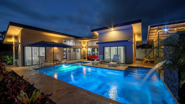 Een modern huis met een zwembad, buitenmeubels en een goed verlicht terras.