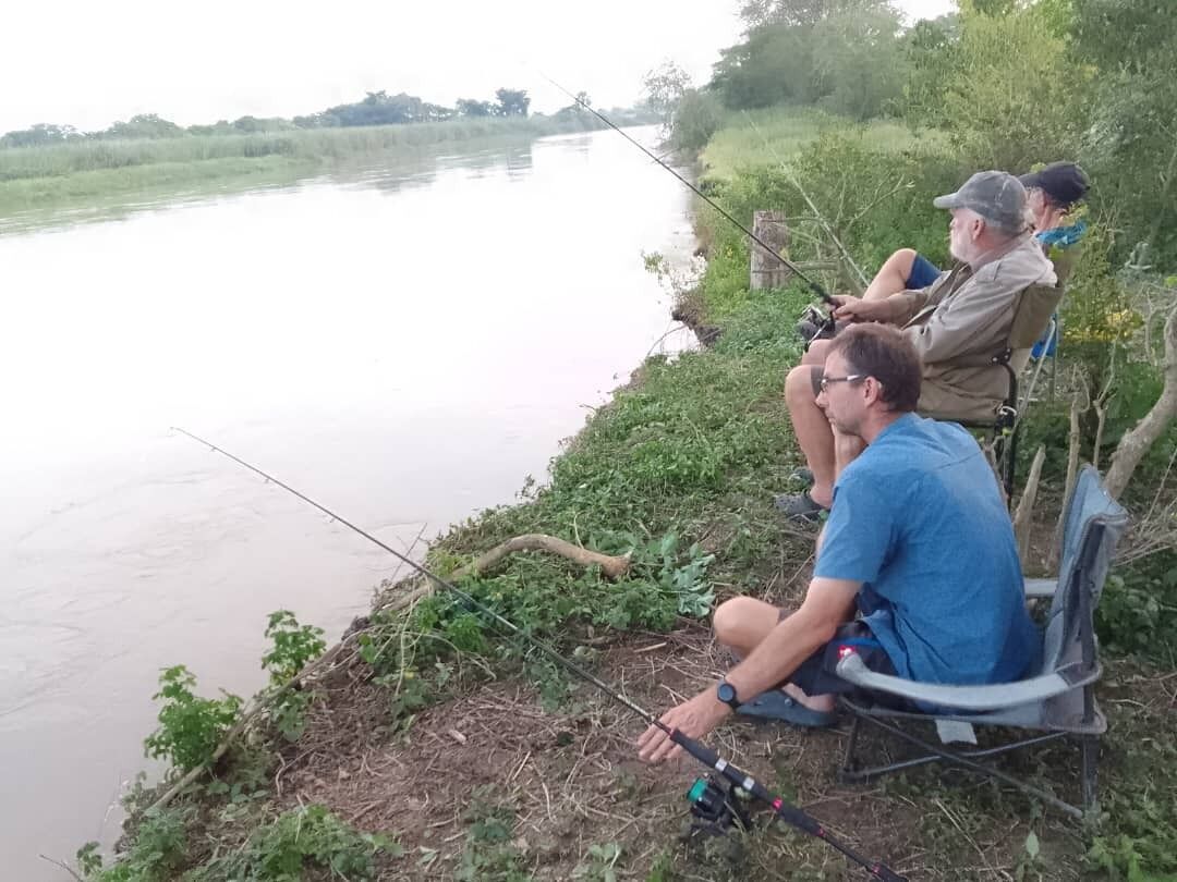 Three people fishing by a calm river.