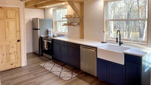 Una cocina moderna con vigas de madera, paredes de azulejos blancos y un ventanal con vistas a un bosque.
