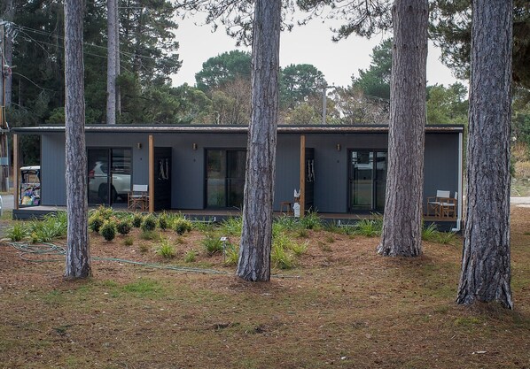 Un edificio moderno de dos pisos con amplias ventanas y techo plano, rodeado de árboles altos.