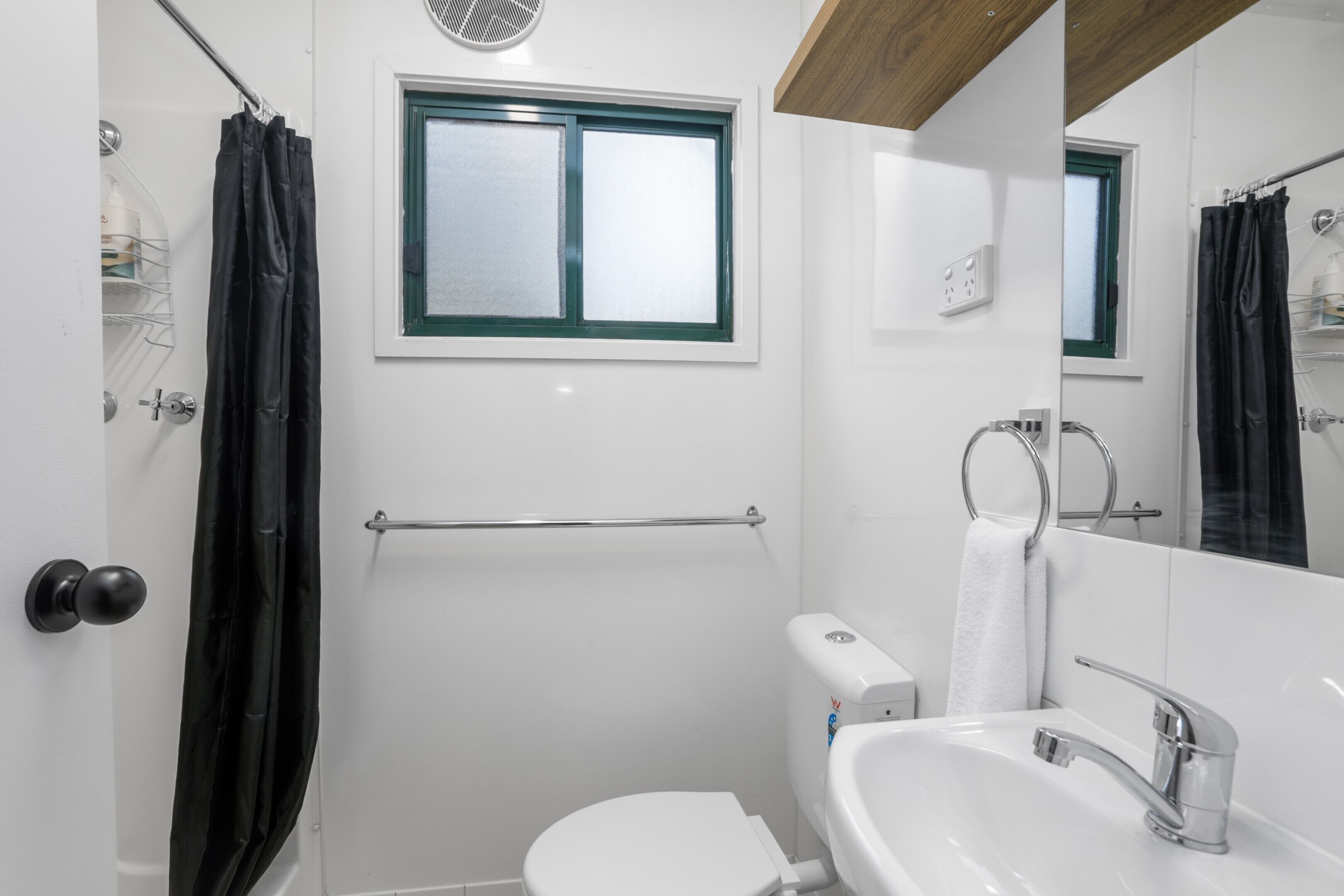 A modern bathroom with a white toilet, a sink with a chrome faucet, a window with a green frame, and a shower curtain.