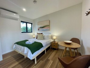 Un dormitorio con cama, mesita de noche, lámpara, sillón y vistas al exterior.