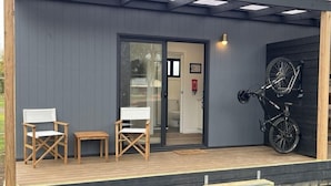 A modern building with a grey exterior, a wooden deck with two chairs, and a bicycle mounted on the wall. - Creswick Holiday Park (Creswick)
