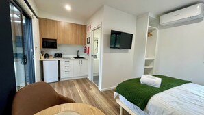 A compact hotel room with a kitchenette, a bed with a green blanket, a TV mounted on the wall, and a small dining area. - Creswick Holiday Park (Creswick)