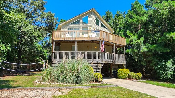 A two-story lodge with a balcony, surrounded by lush greenery and a clear blue sky. - Seas The Day - Oceanside 4 BR Home w/Private Pool - Short walk to shops/restaurants (Duck)