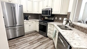 A modern kitchen with white cabinetry, stainless steel appliances, a wood-patterned floor, and a granite countertop.