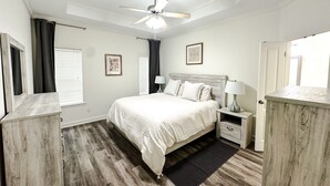 A bedroom with a bed, nightstands, a ceiling fan, and a door.