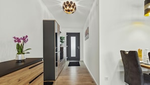 Un couloir moderne avec un banc en bois, une orchidée en pot, une porte grise et un coin repas comprenant une chaise et une table.