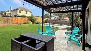 A covered patio with wicker furniture and turquoise chairs, a wooden fence, and a swimming pool in the background. - Villa with Pool, BBQ and More (Flower Mound)