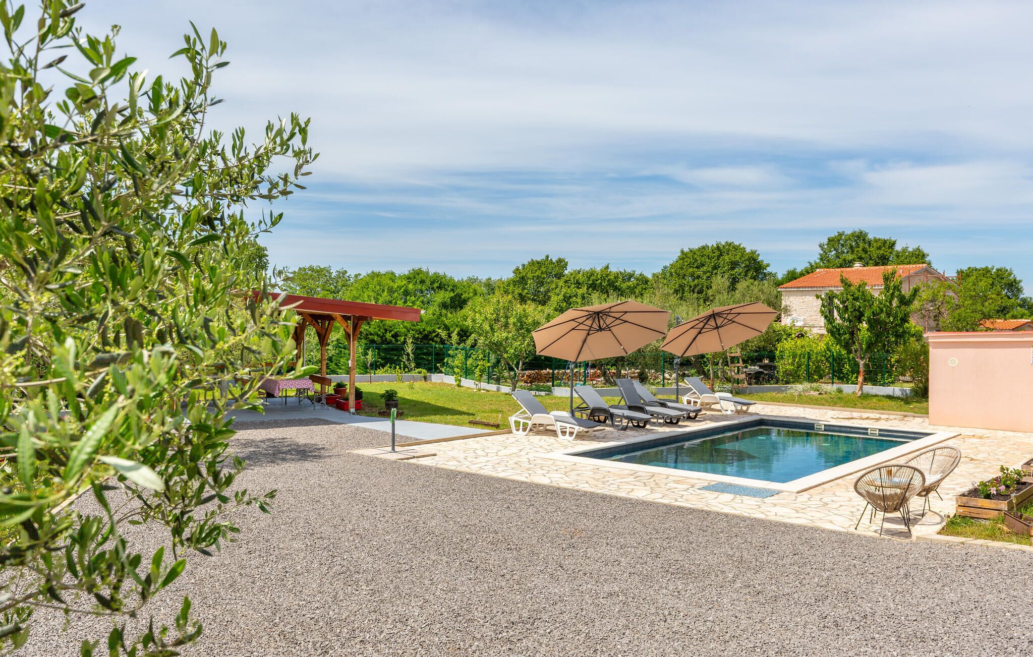Ein Poolbereich mit Liegestühlen und Sonnenschirmen, umgeben von viel Grün und einem Gebäude im Hintergrund.