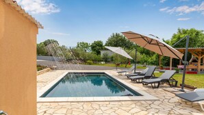 A swimming pool with lounge chairs and umbrellas, surrounded by stone tiles and greenery. - Gorgeous apartment in Malinska with swimming pool (Malinska)