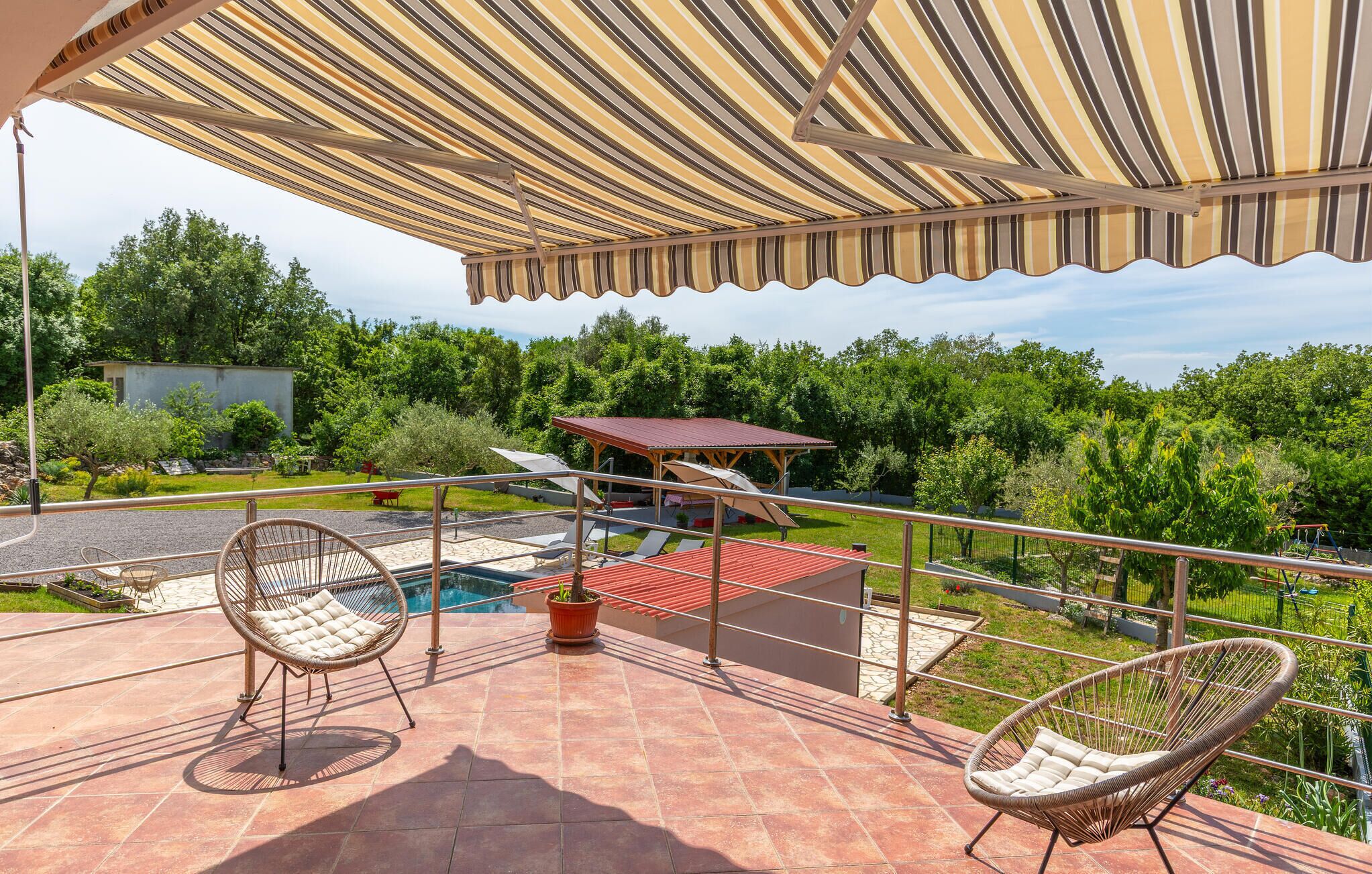 A terrace with two wicker chairs, a pool, and a red-roofed structure.