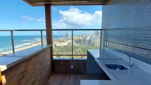 A balcony with a city view, a sink, and a wooden floor. - Vista mar no Costa Azul (Costa Azul Salvador)