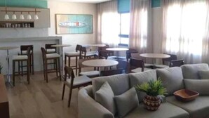 A hotel lobby with a seating area, a bar, and a large window. - Vista mar no Costa Azul (Costa Azul Salvador)