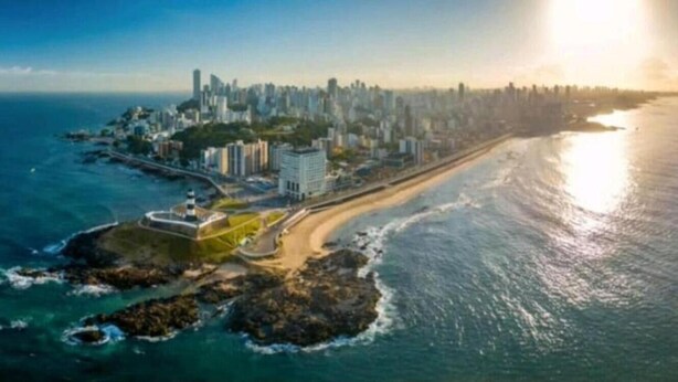 An aerial view of a coastal city with a prominent beach, a marina, and high-rise buildings. - Vista mar no Costa Azul (Costa Azul Salvador)