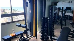 A gym with a bench press, squat rack, and dumbbells. - Vista mar no Costa Azul (Costa Azul Salvador)