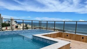 A rooftop infinity pool with a wooden deck and a city view. - Vista mar no Costa Azul (Costa Azul Salvador)
