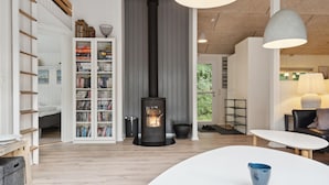 A modern living room with a central fireplace, built-in bookshelves, and a cozy seating area. - Beautiful home in Glesborg with sauna (Glesborg)