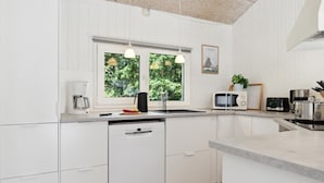 A modern kitchen with white cabinetry, a built-in dishwasher, a double sink, and a window with a view of greenery. - Beautiful home in Glesborg with sauna (Glesborg)