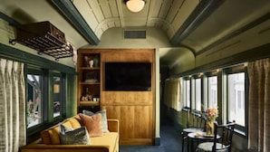A train carriage interior with a wooden panel wall, a sofa, a table with chairs, and a window with curtains. - The Hotel Chalet at The Choo Choo (Chattanooga)