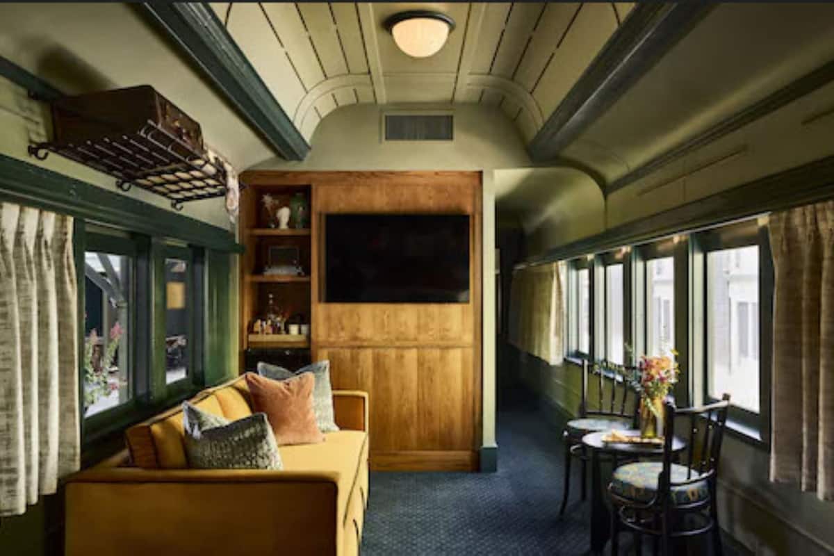 Een treincoupé met houten paneelbekleding, een bank, een tafel met stoelen en een raam met gordijnen.