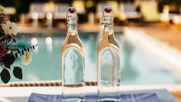 Two empty glass bottles on a table by a poolside with a wooden cabinet below.