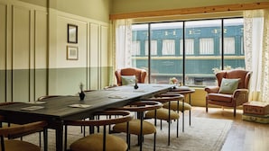 Un espace repas avec une longue table, de nombreuses chaises et une vue sur un train vert qui passe, visible à travers de grandes fenêtres.