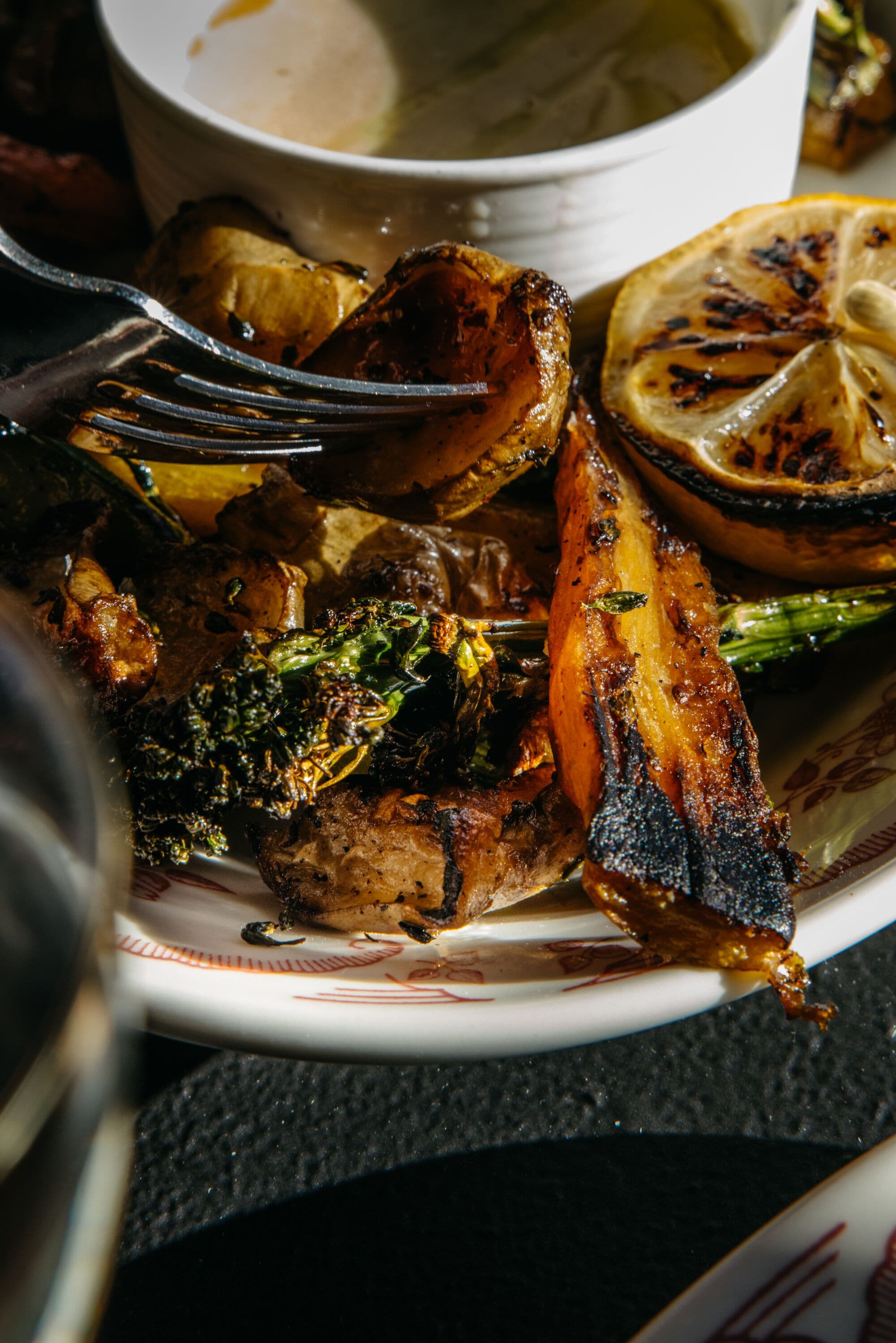 A plate of grilled vegetables and meat, including broccoli and potatoes, served on a white plate with a fork.