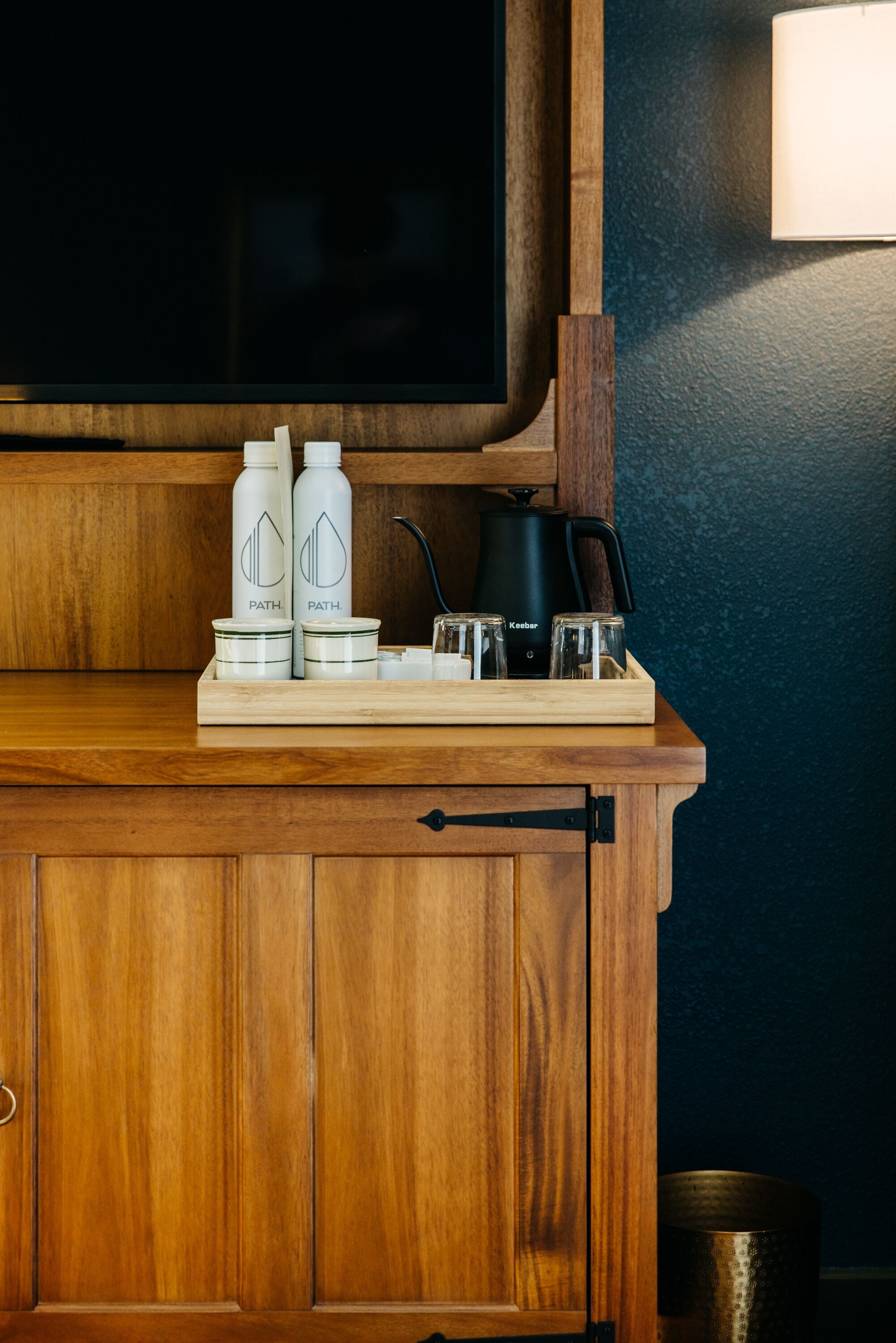 A wooden cabinet with a tray holding two bottles, a jar, and a kettle.
