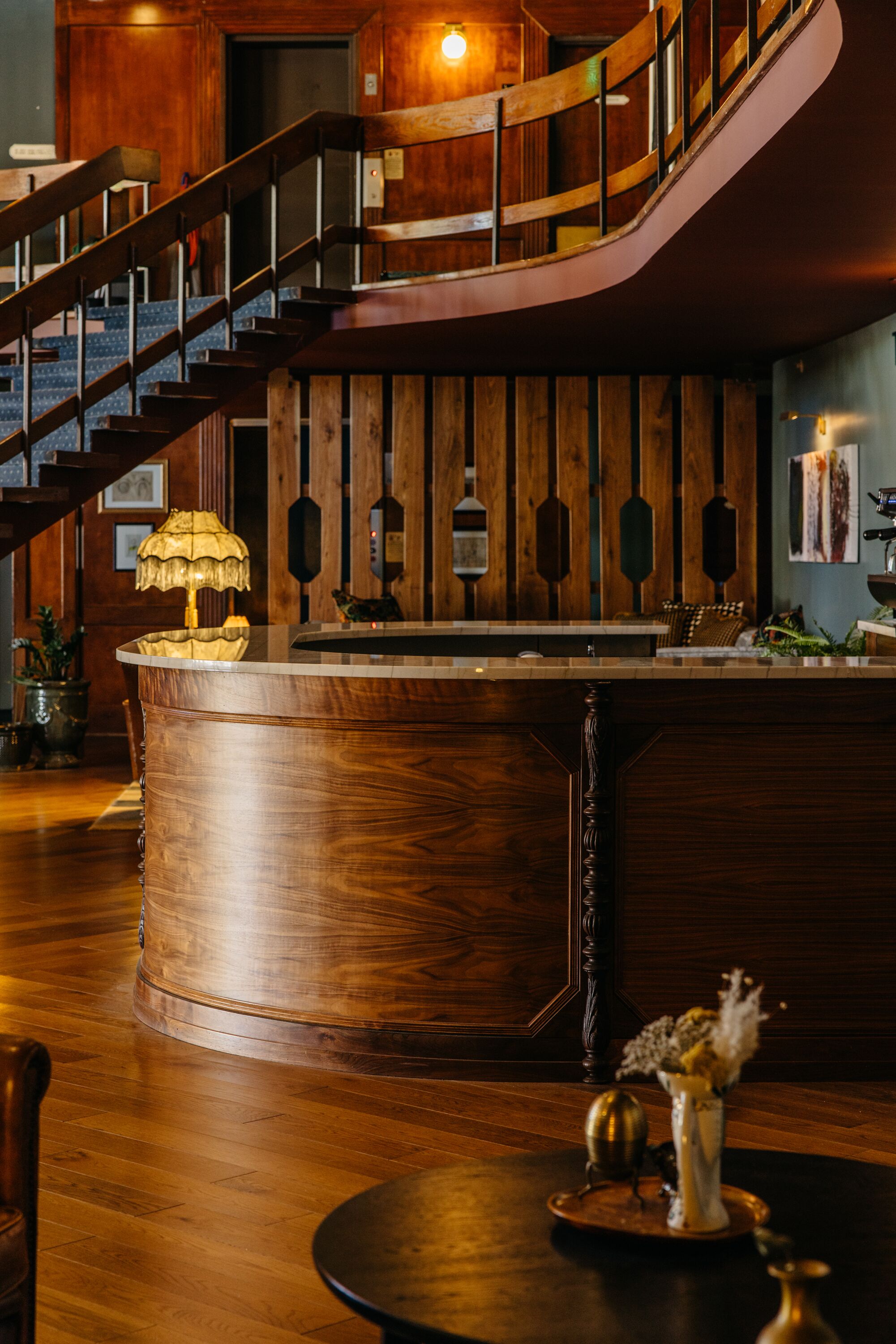 A wooden bar area with a curved counter, a staircase, and a wooden wall with vertical panels.