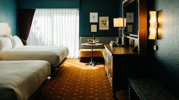Une chambre d’hôtel avec deux lits, une petite table ronde sur laquelle se trouve une bouteille de vin, un banc et un grand miroir.