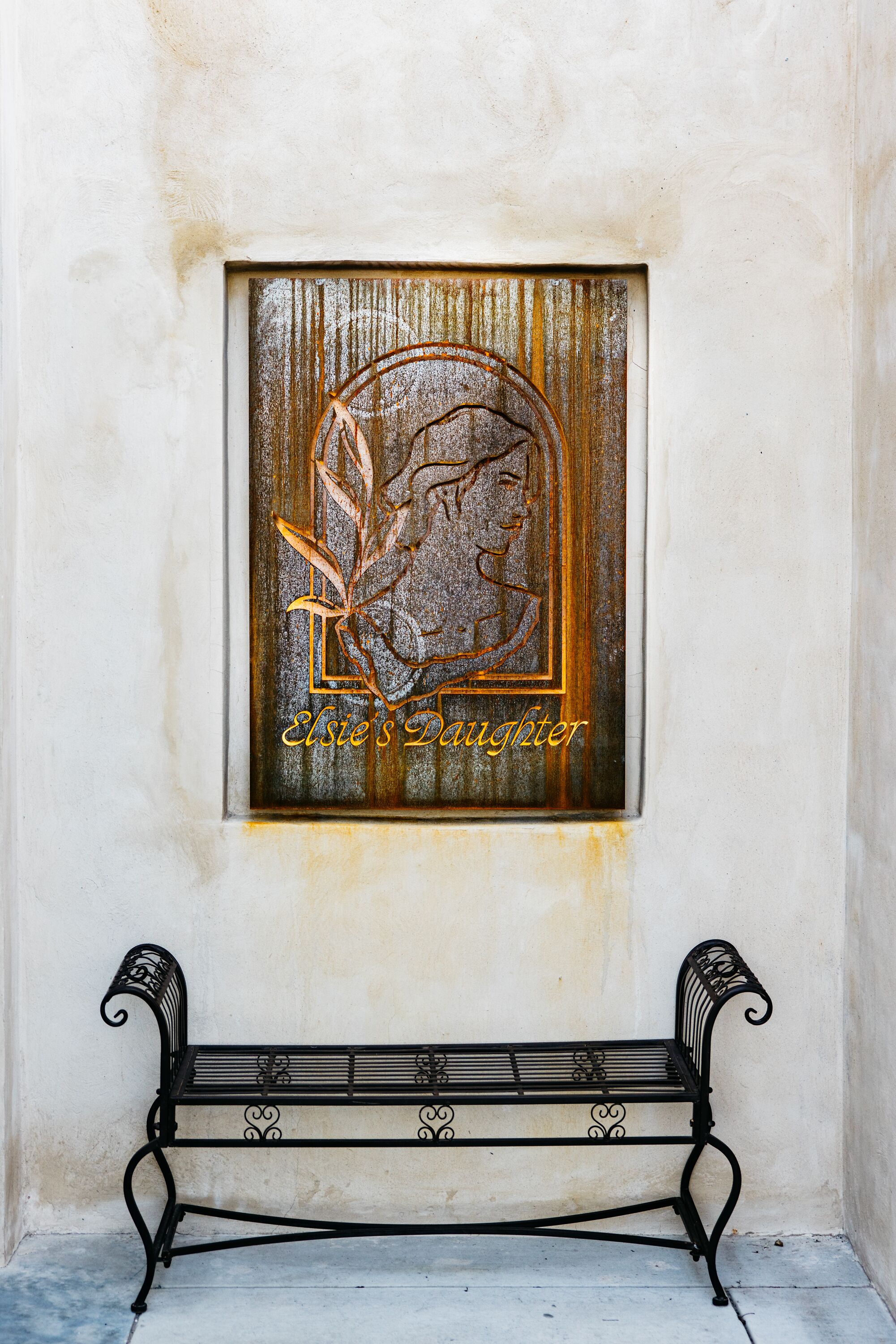 Un banco con una placa decorativa que muestra el perfil de una mujer y la inscripción 'Elsie's Daughter'.