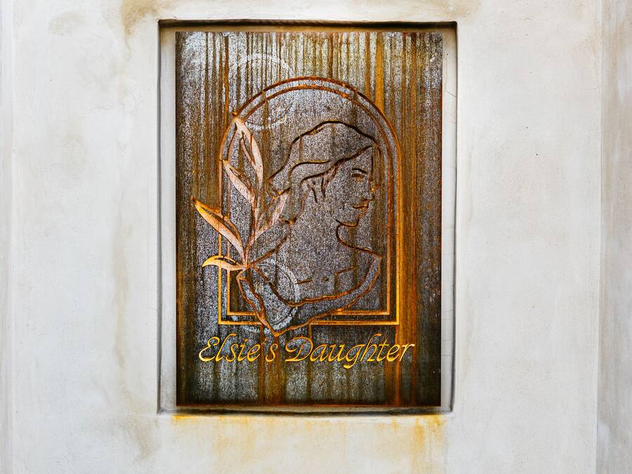 Un banco con una placa decorativa que muestra el perfil de una mujer y la inscripción 'Elsie's Daughter'.