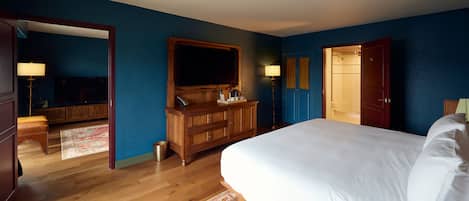 A bedroom with a large bed, wooden dresser, and a TV mounted on the wall.