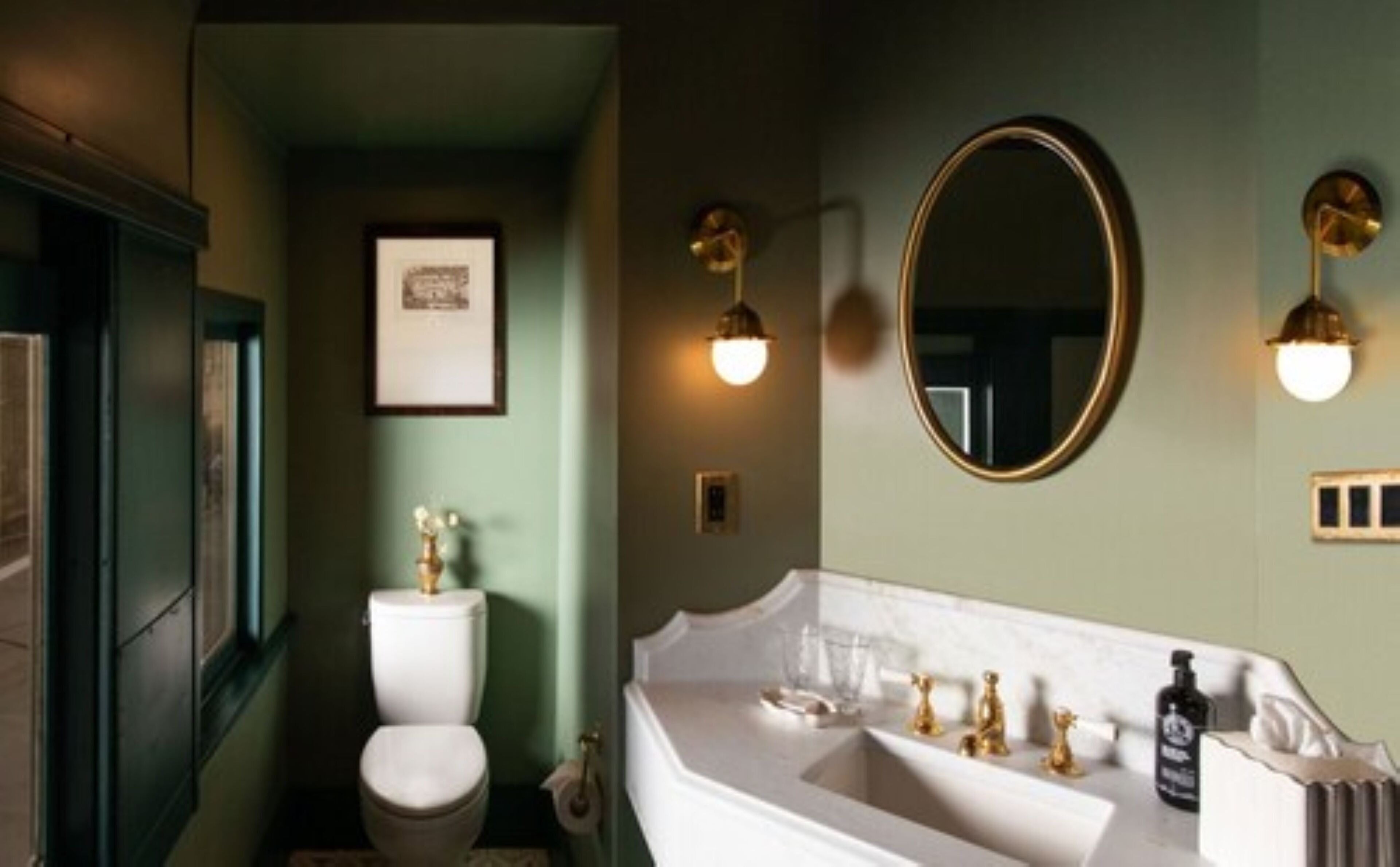 A bathroom with a white sink, gold faucets, and a round mirror.