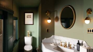 A bathroom with a white sink, gold faucets, and a round mirror.