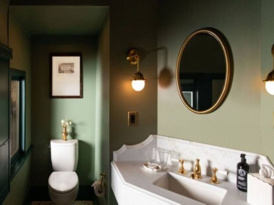 A bathroom with a white sink, gold faucets, and a round mirror.