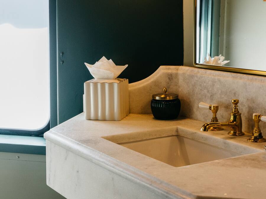 A bathroom with a sink, a tissue box, a black container, and a mirror.