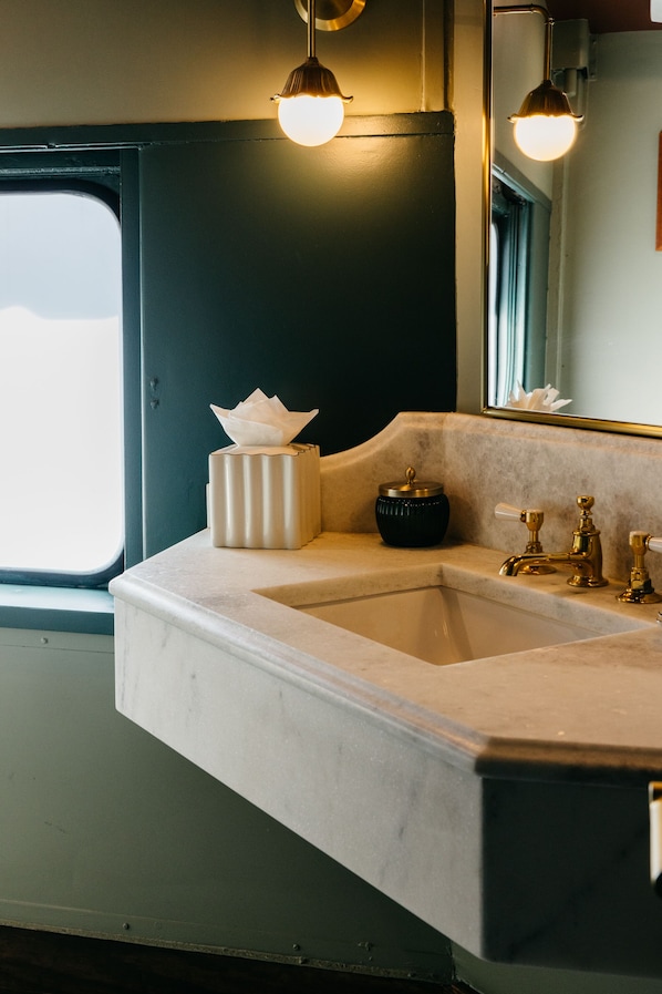 Une salle de bain avec un lavabo, une boîte de mouchoirs, un récipient noir et un miroir.