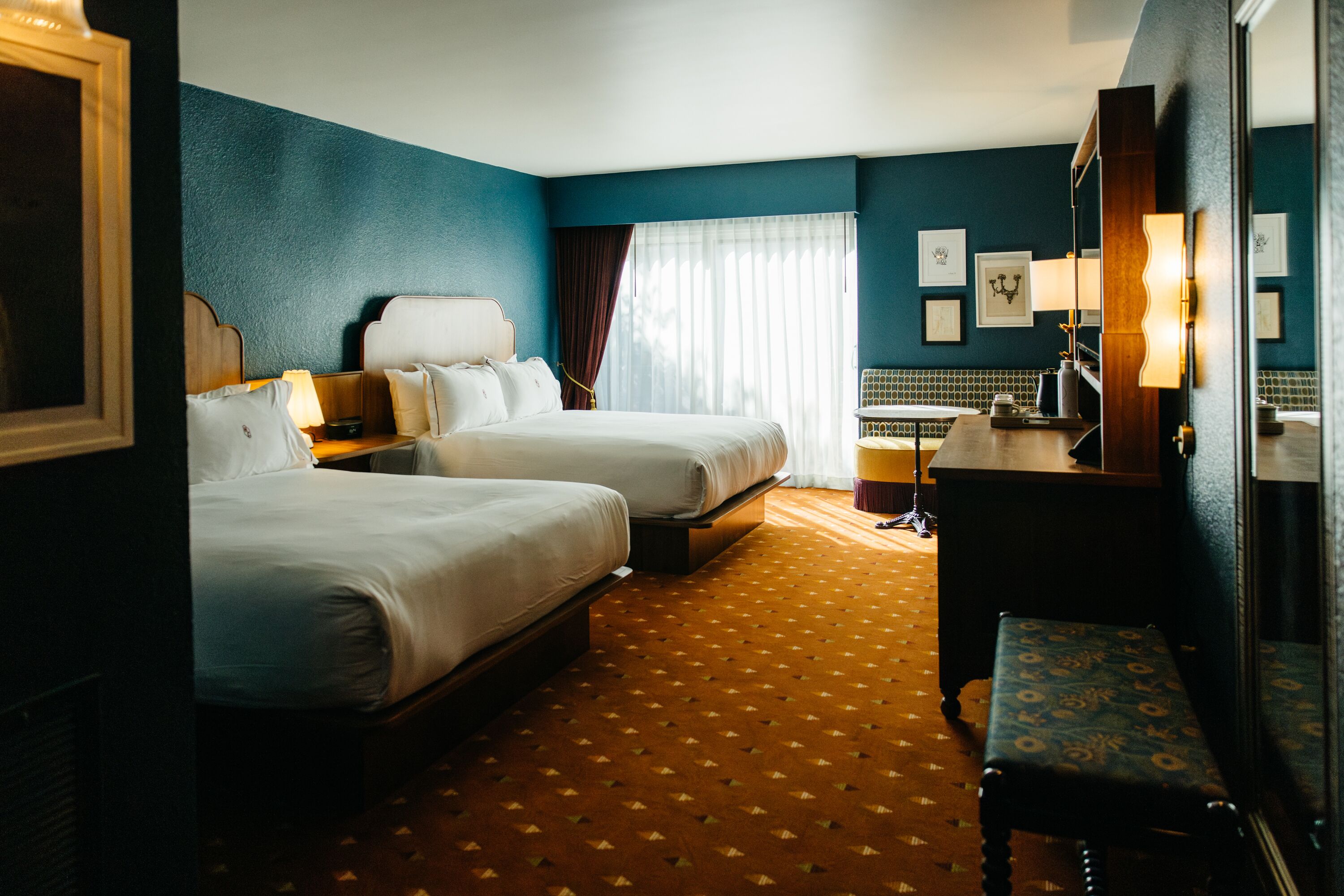 A hotel room with two beds, a desk, a chair, and a bathroom.