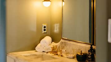 A bathroom with a marble sink, gold fixtures, a large mirror, and a wall-mounted light.