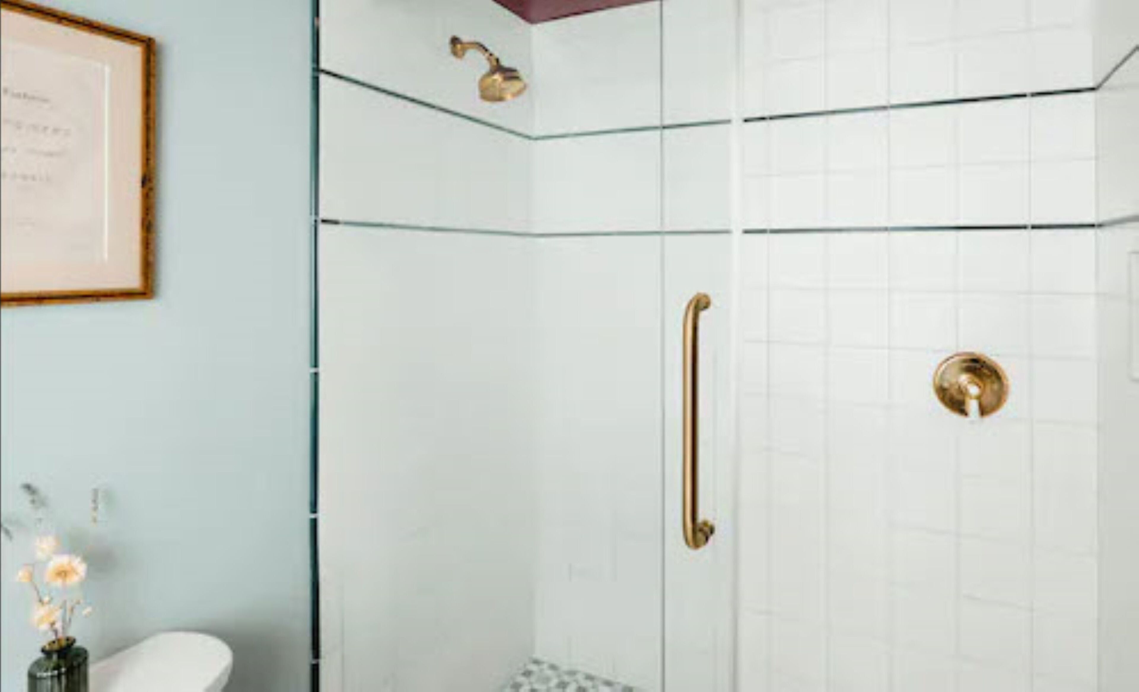 Une salle de bain avec une douche à parois de verre, un certificat encadré accroché au mur et une petite table de chevet sur laquelle est posé un vase de fleurs.