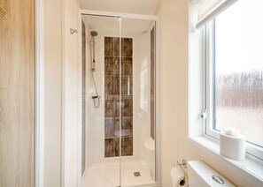 A modern bathroom with a glass-enclosed shower, a toilet, and a window with a view of a snowy landscape. - Sea View Lodge 3 Pet Friendly (Kirkcudbright)