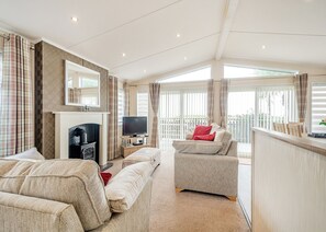 A spacious living room with a fireplace, a television, and a balcony with curtains. - Sea View Lodge 3 Pet Friendly (Kirkcudbright)