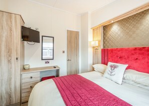 A bedroom with a bed, a dresser, a TV, a window, and a lamp. - Sea View Lodge 3 Pet Friendly (Kirkcudbright)